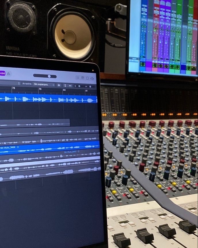 Mixing session on a laptop next to a large analog mixing console and studio monitors